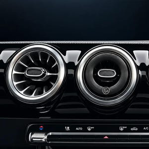 Könnte beinhalten: Ein Auto-Armaturenbrett mit drei runden Lüftungsdüsen, die mit silbernen Metallrändern und schwarzen Lamellen versehen sind. Die mittlere Düse zeigt ein kleines kreisförmiges Logo mit den Buchstaben FM. Darunter befindet sich eine Bedienleiste.
