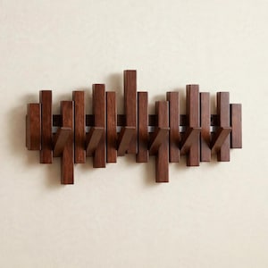 May include: A wall-mounted coat rack constructed from dark brown wood, featuring a series of vertical rectangular slats of varying heights. Several of these slats are angled outward to function as hooks for hanging items, creating a rhythmic pattern.
