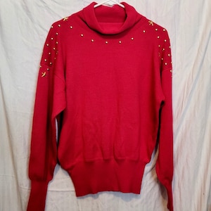 May include: A red turtleneck sweater with gold star and dot embellishments.