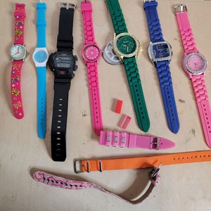 May include: Collection of colorful wristwatches with various band styles and face designs. Includes watches with pink, blue, green, and black bands. Some watches have rhinestone accents and butterfly details.