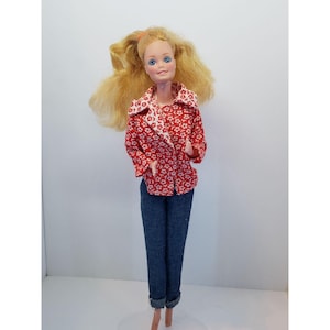 May include: A vintage doll with long blonde hair, blue eyes, and a red floral print jacket over a white floral print top. The doll is wearing blue denim jeans with rolled-up cuffs.