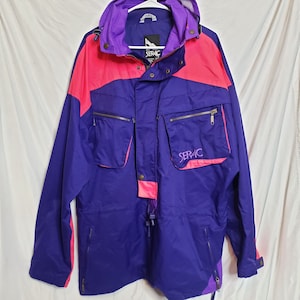 May include: A vintage purple, pink, and violet SERAC jacket. The jacket features a hood, multiple zippered pockets, and the SERAC logo on the front. The jacket has a drawstring at the waist and a zipper closure. The jacket is made of a lightweight material.