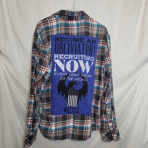 May include: A grey, blue and white plaid flannel shirt with a blue patch on the back. The patch has the text "Become an Obliviator! Recruiting Now Every Half Moon of the Month!" and a black and white eagle with a banner that says "MACUSA".