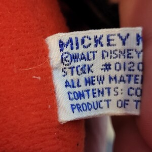 Peut inclure: Une &eacute;tiquette blanche avec du texte bleu qui dit "MICKEY MOUSE WALT DISNEY STOCK #0120 ALL NEW MATERIAL CONTENTS: COTTON PRODUCT OF TAIWAN".