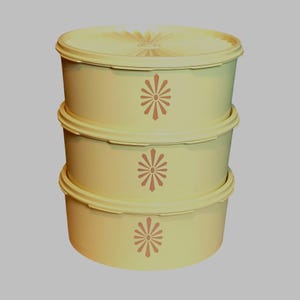 Puede incluir: Tres recipientes de plástico amarillo con tapas apilados uno encima del otro. Cada recipiente tiene un diseño de flor estilizado marrón.