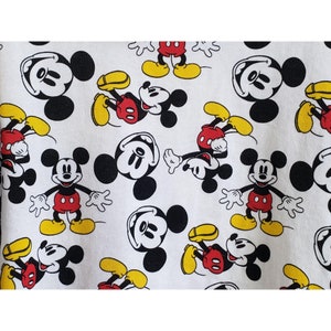 May include: White fabric with a repeating pattern of Mickey Mouse. Mickey Mouse is depicted in black and white with red shorts and yellow shoes.