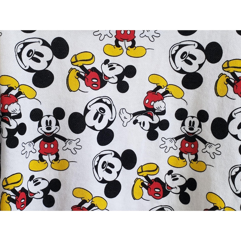 May include: White fabric with a repeating pattern of Mickey Mouse. Mickey Mouse is depicted in black and white with red shorts and yellow shoes.