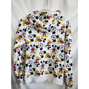 May include: White hooded sweatshirt with a full-coverage print of Mickey Mouse in various poses. The print features Mickey Mouse in black, red, and yellow.