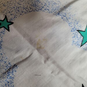 May include: White fabric with a blue and green star pattern. There are a few brown stains on the fabric.