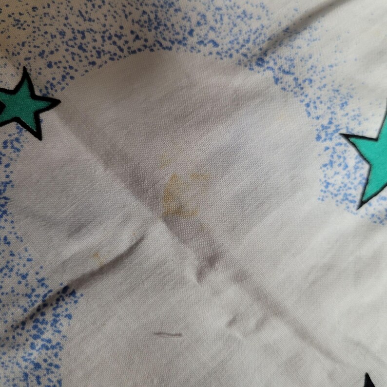 May include: White fabric with a blue and green star pattern. There are a few brown stains on the fabric.