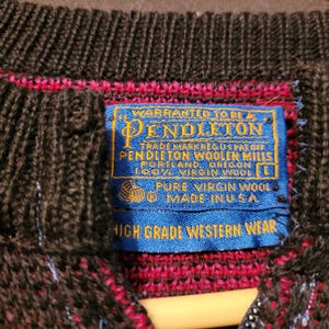 K&ouml;nnte beinhalten: Nahaufnahme eines dunkelbraunen und roten Pendleton-Wollpullovers. Das blaue Etikett lautet: "Pendleton Woolen Mills, Portland, Oregon, 100% Virgin Wool, Pure Virgin Wool, Made in USA, High Grade Western Wear."