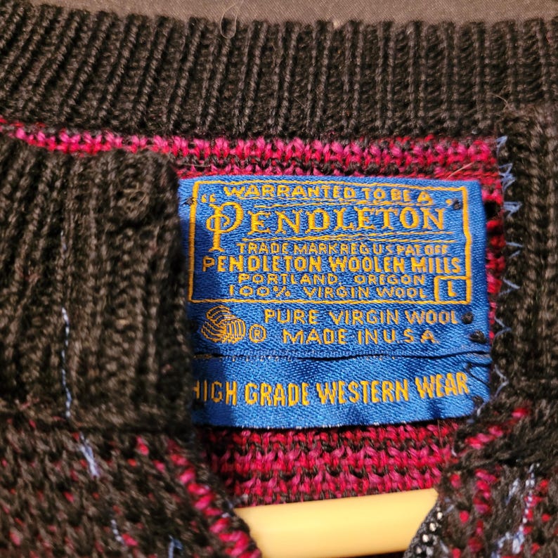 K&ouml;nnte beinhalten: Nahaufnahme eines dunkelbraunen und roten Pendleton-Wollpullovers. Das blaue Etikett lautet: "Pendleton Woolen Mills, Portland, Oregon, 100% Virgin Wool, Pure Virgin Wool, Made in USA, High Grade Western Wear."