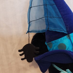K&ouml;nnte beinhalten: Ein blauer und schwarzer Hexenhut mit einem blauen und wei&szlig;en Tupfenmuster und einer schwarzen Spinne, die am Rand h&auml;ngt.