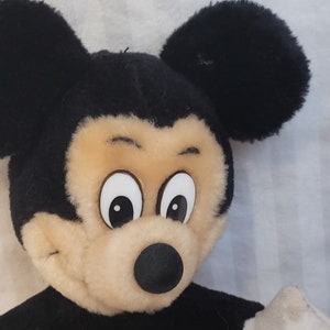 Puede incluir: Un juguete de peluche Mickey Mouse negro y marr&oacute;n con grandes ojos blancos y una nariz negra. El juguete est&aacute; mirando hacia la derecha.