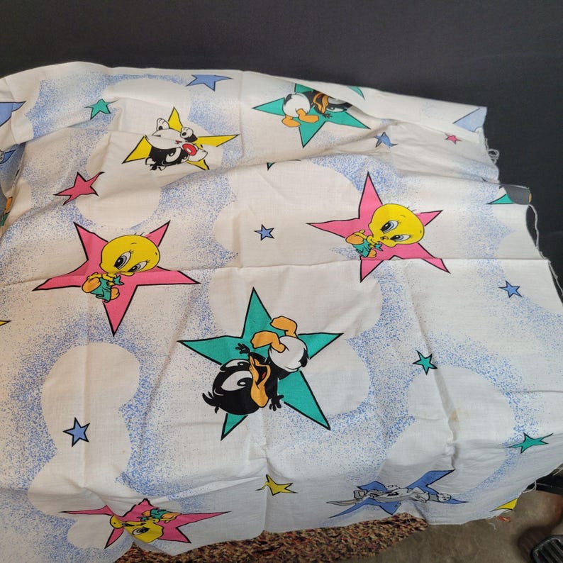 May include: White fabric with a repeating pattern of cartoon characters Tweety Bird and Daffy Duck in stars. The background is white with blue and light blue swirls and stars.