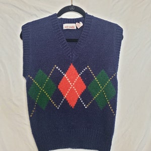 Puede incluir: Un chaleco de punto azul marino con cuello en V y un patrón de rombos en rojo, verde, blanco y amarillo. El chaleco tiene una etiqueta que dice "vicky vanessa".