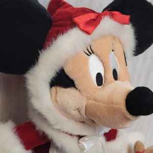 K&ouml;nnte beinhalten: Ein Pl&uuml;schtier von Minnie Mouse, die ein rot-wei&szlig;es Weihnachtsmannkost&uuml;m mit einer roten Schleife tr&auml;gt. Sie hat schwarze Augen und ein wei&szlig;es Gesicht.