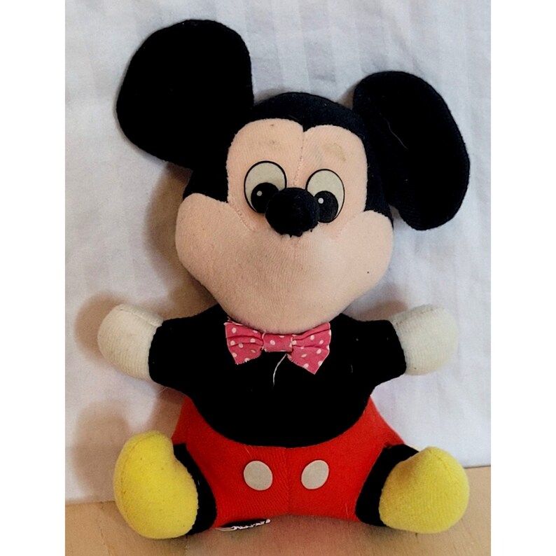 Peut inclure: Un jouet en peluche Mickey Mouse avec des oreilles noires, une tenue noire et rouge et un n&oelig;ud papillon rose &agrave; pois blancs.