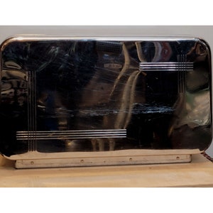 May include: A silver metal box with a decorative pattern of lines. The box has a slightly rounded top and a flat bottom.