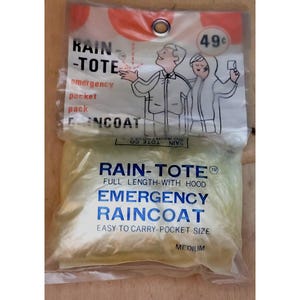 May include: A yellow plastic pouch containing a blue and white emergency raincoat. The pouch has the text "RAIN-TOTE" and "EMERGENCY RAINCOAT" printed on it. The raincoat is full length with a hood and is easy to carry in a pocket.