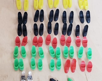 May include: A collection of colourful plastic shoes in various styles and colours, including black, green, yellow, and red. The shoes are arranged in rows on a light wood surface.