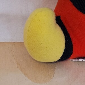Peut inclure: Gros plan sur un jouet en peluche avec un motif jaune, rouge et noir. Le jouet a une forme ronde et duveteuse.