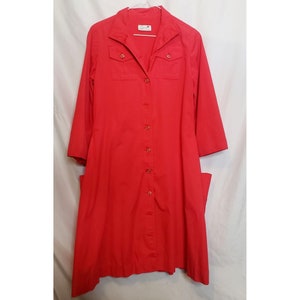 Puede incluir: Un vestido rojo de botones de manga larga con dos bolsillos grandes a los lados. El vestido tiene un cuello y un frente abotonado.