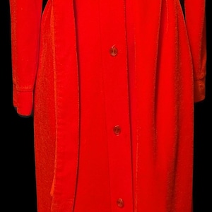 May include: A long, vibrant red dress with a matching belt. The dress features a V-neckline, long sleeves, and a button-down front. The fabric appears to be a soft velvet or velour.
