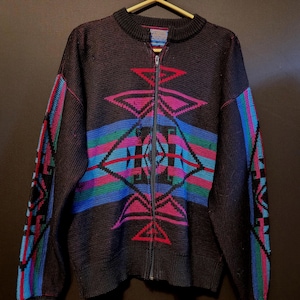 K&ouml;nnte beinhalten: Dunkelbraune Strickjacke mit Rei&szlig;verschluss und geometrischem Muster in Rosa, Blau, Gr&uuml;n und Rot. Die Strickjacke hat einen gerippten Kragen und B&uuml;ndchen, und das Muster wiederholt sich auf den &Auml;rmeln. Der Rei&szlig;verschluss ist silberfarben.