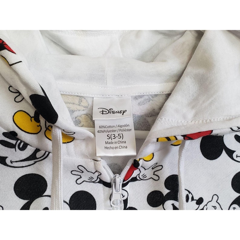 May include: White hooded sweatshirt with a full-color Mickey Mouse print. The sweatshirt has a zipper closure and the tag says "Disney" with the fabric content and size information: 60%Cotton/Algod&oacute;n 40%Polyester/Poli&eacute;ster S(3-5) Made in China Hecho en China