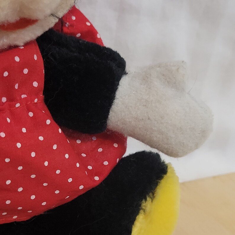 Puede incluir: Un juguete de peluche de un personaje de dibujos animados que lleva un vestido rojo con lunares blancos, zapatos negros y guantes blancos. El juguete est&aacute; hecho de tela suave y peluda.