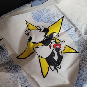 May include: A white fabric with a yellow star and a black and white cartoon character. The character is a bird with large eyes and a red beak. The character is riding on the star.