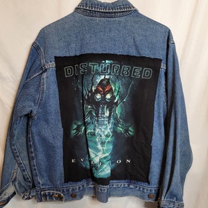 May include: A blue denim jacket with a black patch featuring the band Disturbed and the album title "Evolution". The patch has a graphic of a creature with a gas mask and glowing green eyes.