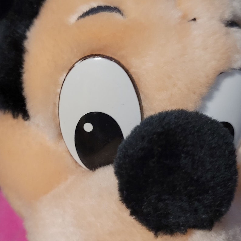 Op de afbeelding: Close-up van het gezicht van een pluche speelgoed, met een groot wit oog met een zwarte pupil en een zwarte neus. De vacht van het speelgoed is lichtbruin.