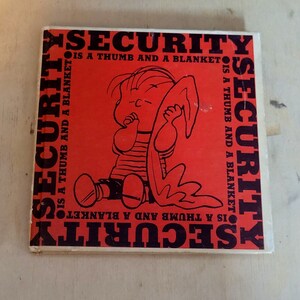 May include: A red book with the text "SECURITY IS A THUMB AND A BLANKET" repeated on all sides. The cover features a cartoon illustration of a child holding a blanket.