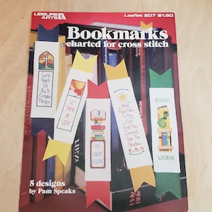 May include: A booklet titled "Bookmarks charted for cross stitch" featuring five different bookmark designs. The designs include a bookworm, a book with a sun, a book with a cross, a book with a sunrise, and a book with a quote about light.