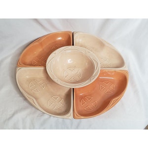 Puede incluir: Un juego de servir de cerámica con un cuenco central y cuatro platos en forma de cuña. El juego presenta una cálida paleta de colores melocotón y crema, con diseños de cruces en relieve. Ideal para servir aperitivos.