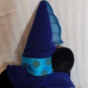 K&ouml;nnte beinhalten: Schwarzes Pl&uuml;schtier, das einen blauen und t&uuml;rkisfarbenen Zaubererhut mit einer spitzen Spitze und einem blauen und t&uuml;rkisfarbenen Band mit wei&szlig;en Punkten tr&auml;gt.