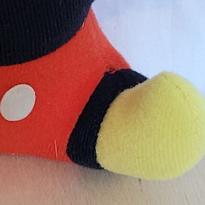Peut inclure: Gros plan sur un jouet en peluche rouge, noir et jaune avec un cercle blanc sur le tissu rouge. Le jouet est un personnage avec un pied jaune.
