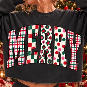 以下が含まれることがあります： 胸元にMERRYの大きなブロック体文字がプリントされたチャコールグレーの長袖スウェットシャツ。各文字には、タータンチェック、赤と緑の市松模様、花柄、赤と緑の水玉模様といったユニークなパターンが施されています。