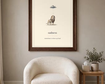 May include: A framed wall art print featuring a drawing of a lion standing under a small rain cloud. Below the lion, the text reads "sadness" followed by the phrase "sometimes it shows up loud" in a clean, black serif font.