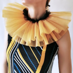 Op de afbeelding: Een gele tule ruchekraag met een zwart lint. De kraag wordt gedragen over een zwart-wit gestreept shirt met gele accenten.