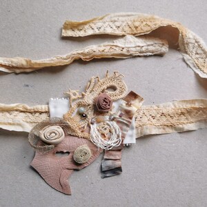 Peut inclure: Une garniture en dentelle beige avec un embellissement en cuir brun et en dentelle. L'embellissement pr&eacute;sente une fleur brune, une perle blanche et un motif tiss&eacute; brun et blanc.