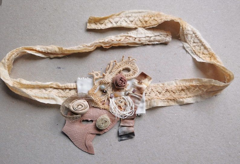 Peut inclure: Une garniture en dentelle beige avec un embellissement en cuir brun et en dentelle. L'embellissement pr&eacute;sente une fleur brune, une perle blanche et un motif tiss&eacute; brun et blanc.