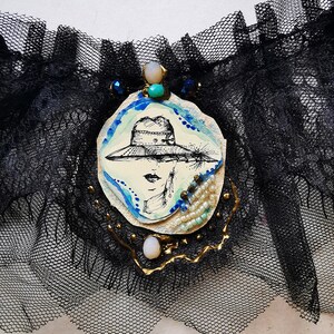 K&ouml;nnte beinhalten: Ein schwarzes Spitzenstrumpfband mit einem wei&szlig;en ovalen Kamee, das eine Frau mit Hut zeigt. Das Kamee ist mit blauen und t&uuml;rkisfarbenen Perlen und goldenen Akzenten verziert.