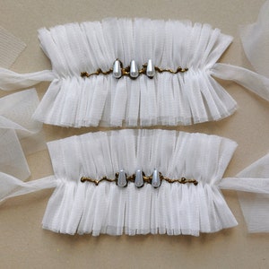 May include: Two white tulle wrist cuffs with gold embellishments and pearl-like accents.