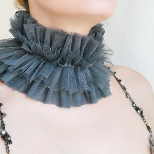 May include: A gray ruffled tulle choker necklace. The choker is made of multiple layers of tulle and is gathered at the back of the neck.