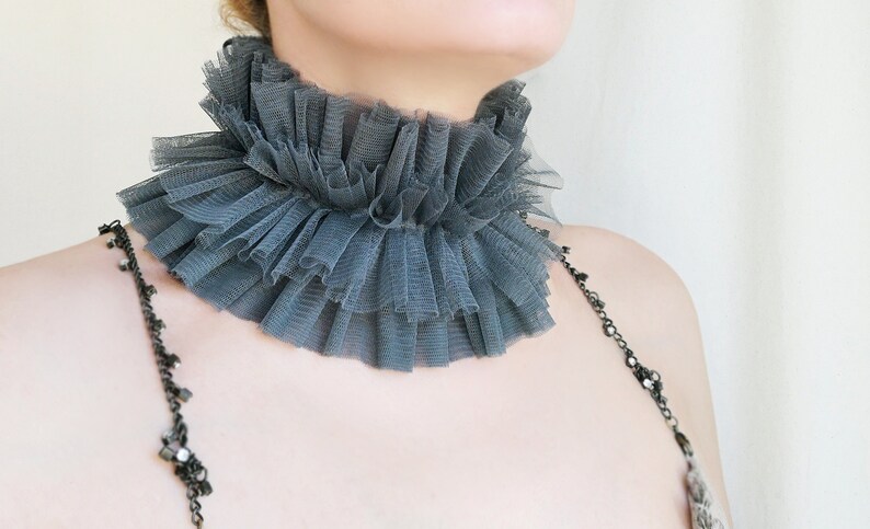 May include: A gray ruffled tulle choker necklace. The choker is made of multiple layers of tulle and is gathered at the back of the neck.