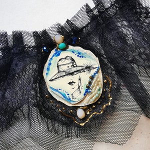 K&ouml;nnte beinhalten: Eine schwarze Spitzen-Choker-Kette mit einem wei&szlig; und blau bemalten Kamee, das eine Frau mit Hut zeigt. Der Kamee ist mit Goldfarbe, Perlen und einem t&uuml;rkisfarbenen Stein verziert.