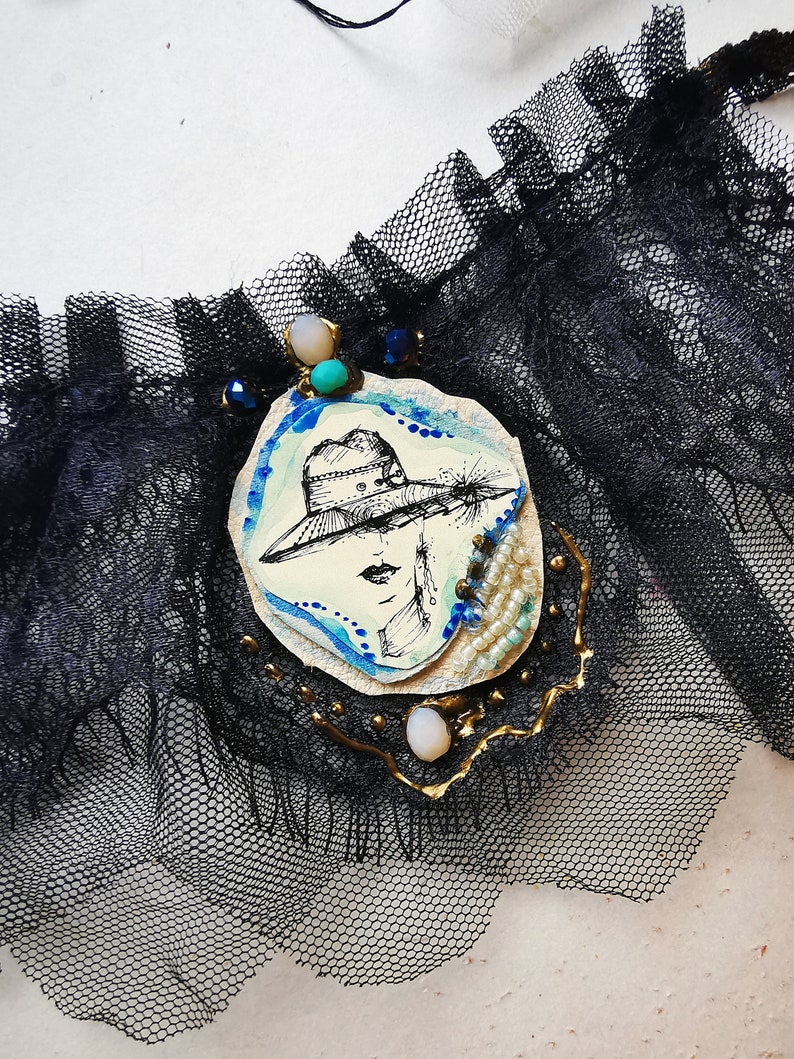 K&ouml;nnte beinhalten: Eine schwarze Spitzen-Choker-Kette mit einem wei&szlig; und blau bemalten Kamee, das eine Frau mit Hut zeigt. Der Kamee ist mit Goldfarbe, Perlen und einem t&uuml;rkisfarbenen Stein verziert.